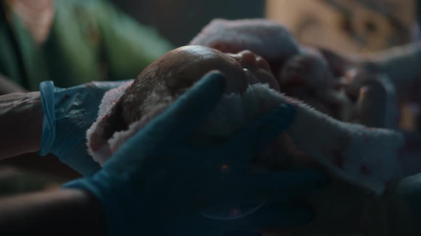 A newborn is placed and held in a blanket in a hospital setting after birth