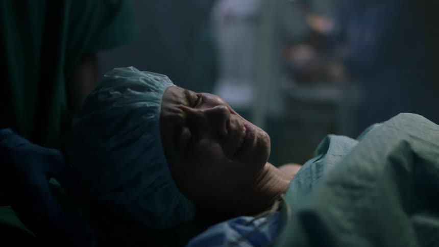 A woman lies on a gurney crying in an operating room as an oxygen mask is placed on her face by medical personnel