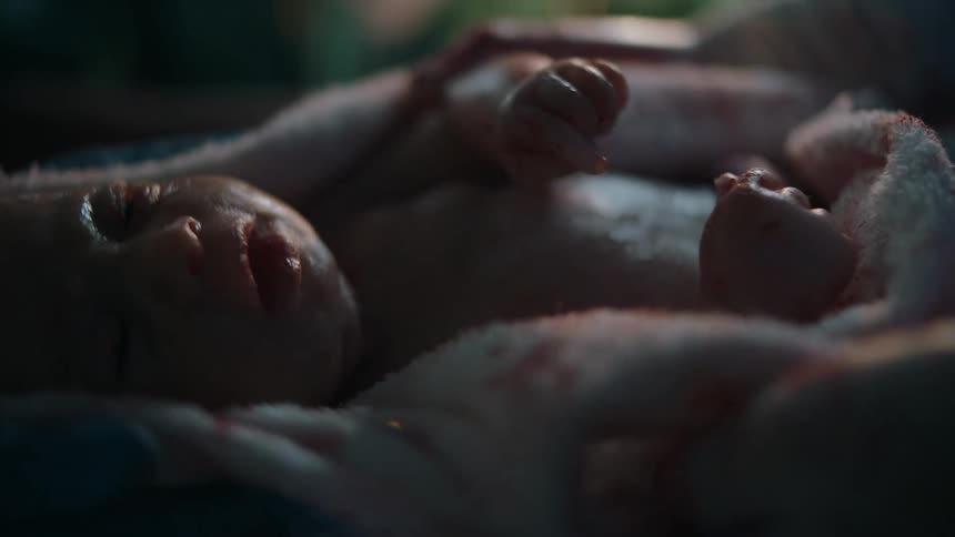 A gloved nurse strokes the forehead of a newborn baby with their thumb
