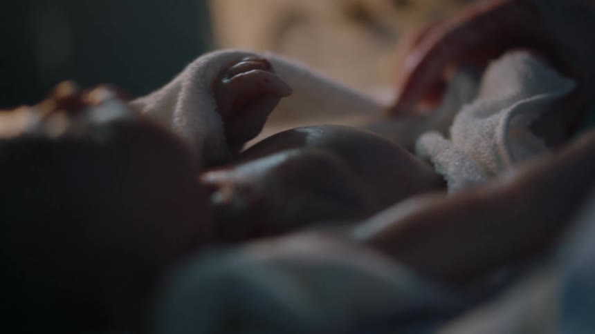 A newborn wrapped in a blanket is being given an oxygen mask