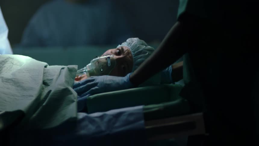 A female lays on her back surrounded by a surgical team in a darkened room
