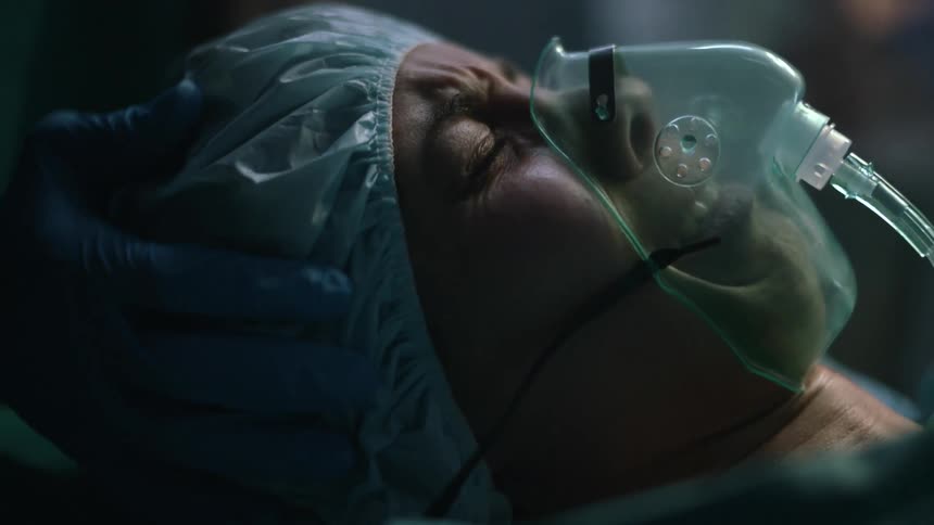 A person holds a woman as she cries and looks over at medical staff working on her newborn baby