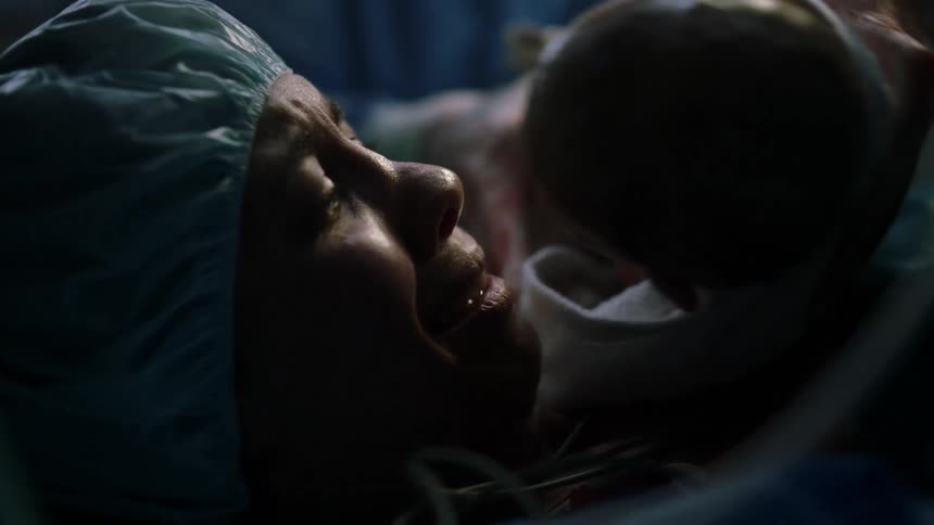A mother is handed her newborn baby as she lies on a gurney in a hospital operating room