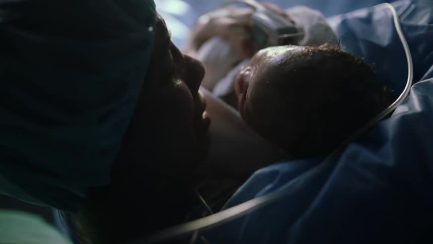 A woman lying in a hospital bed kisses her newborn baby on the head
