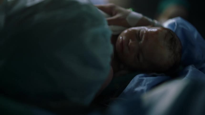 Nurse with a surgical round bouffant cap holds a newborn baby in the hospital