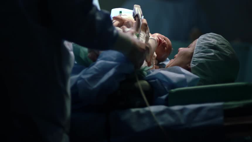A nurse hands a newborn baby to her mother on the operating table