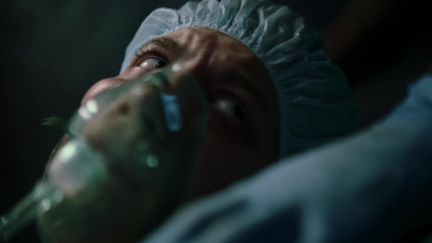 A patient in an operating room turns her head with worry while wearing an oxygen mask