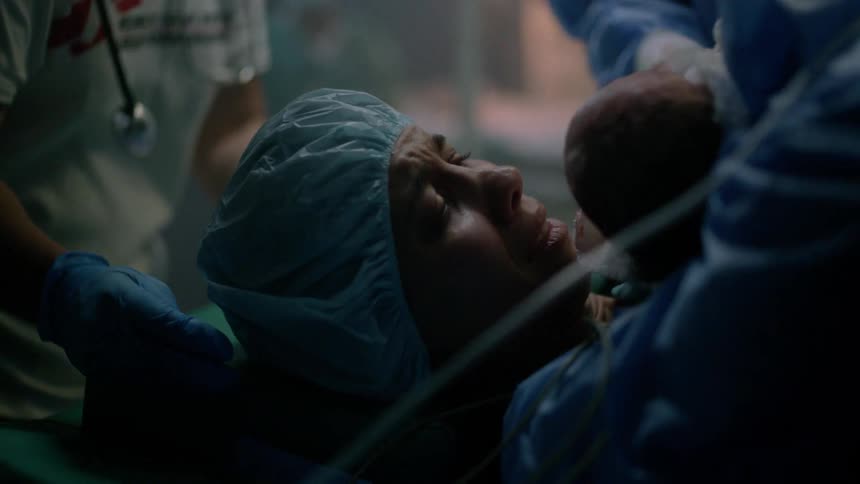 Mother with a surgical round bouffant cap holds the newborn baby and cries tears of joy in the hospital