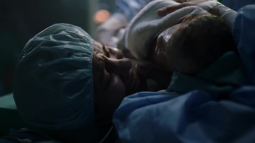A woman is handed her newborn baby in a surgical hospital room