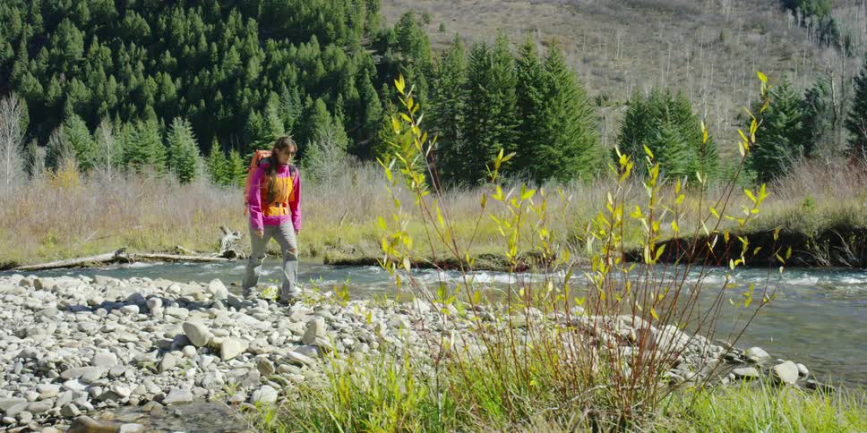 A woman in a pink shirt walks next to a river