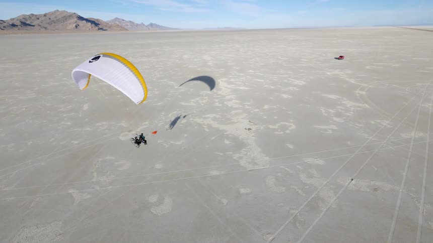 People parachute behind a truck over a long stretch of land