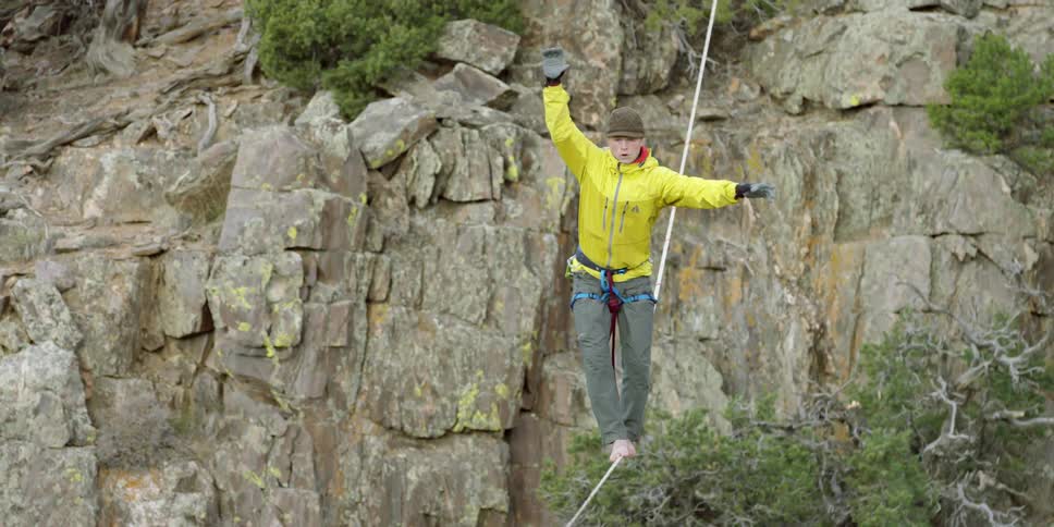 A woman carefully balances on a rope stretched over a gorge