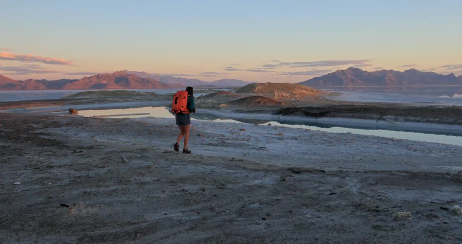 A woman wearing an orange backpack walks over a rocky surface