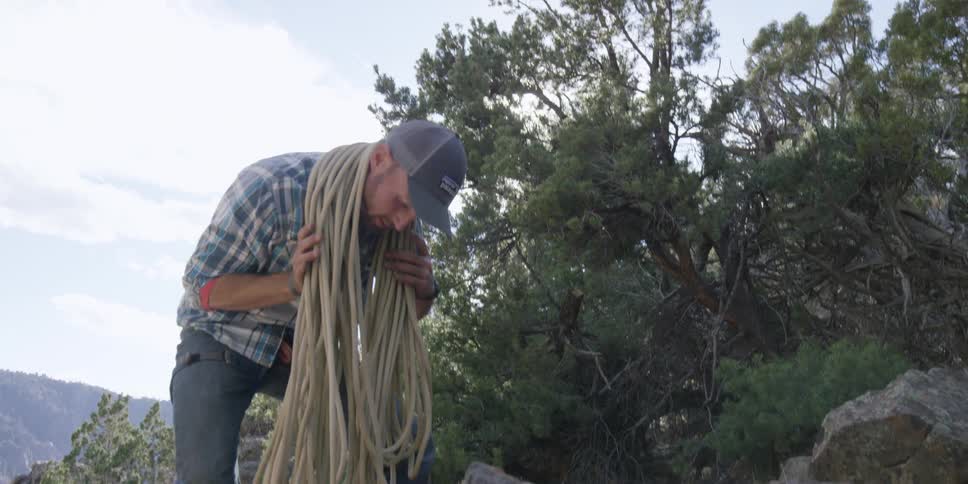 A man gathers a rope by wrapping it over his shoulders