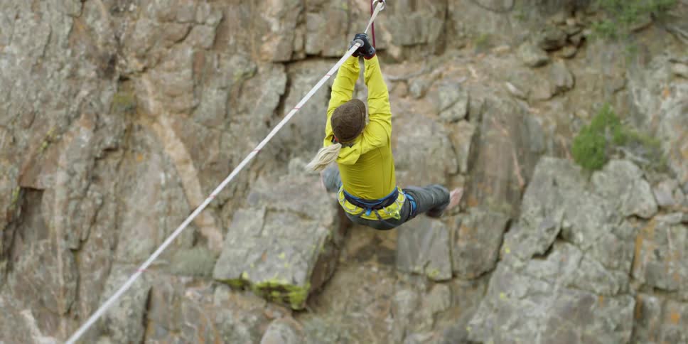 A man walking on a tightrope falls and catches himself hanging