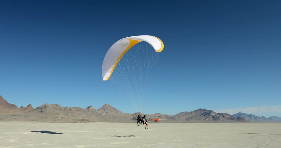 Two people running and lifting a parasail into the air and floating off