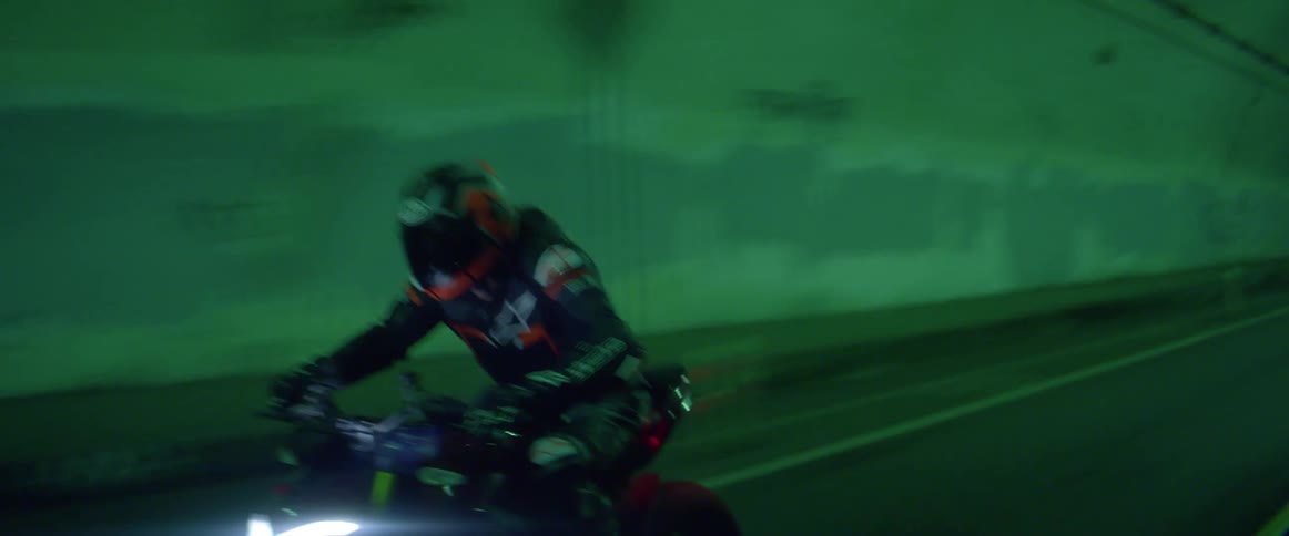 A man speeds through a green painted tunnel on his motorcycle