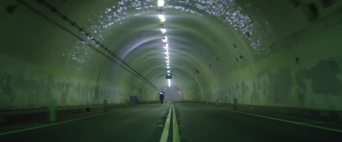 Motorcyclist rides along long tunnel lit by ceiling lights popping a wheelie