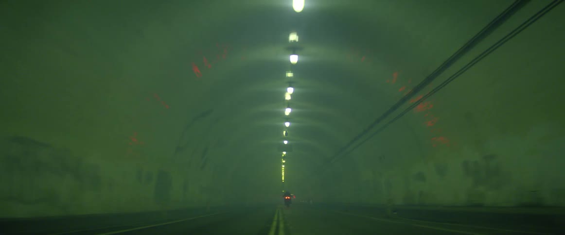 A motorcyclist drives quickly along a road that passes through a tunnel