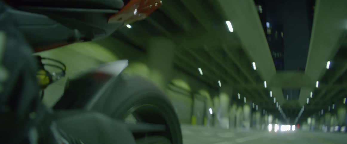 A motorcyclist riding beneath an overpass in a city at night