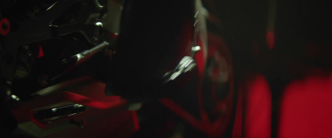 Person pushes foot pedal on motor cycle with red lights in the background