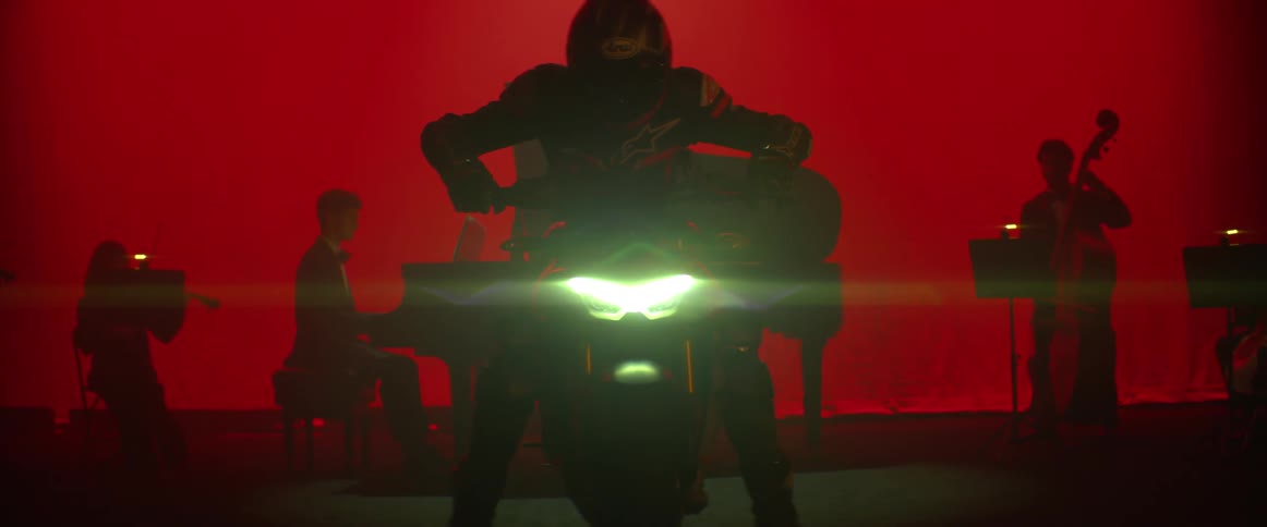 A person starts a motorcycle on a stage in front of three musicians