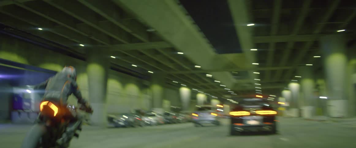 A motorcyclist in a leather jacket weaves through traffic in a long tunnel