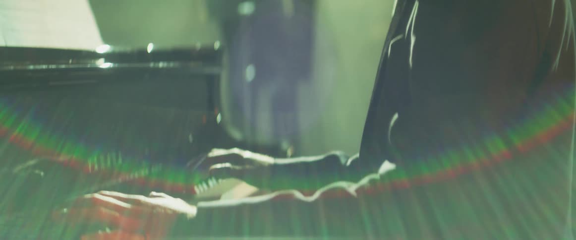 Pianist sitting in front of a grand piano on stage places his hands over the keyboard