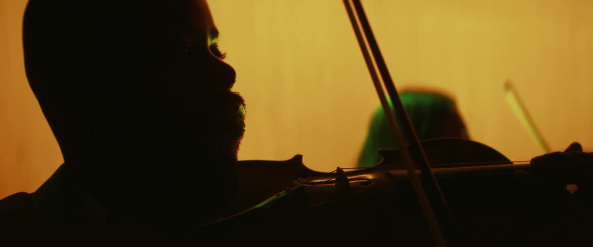 Man positions a violin to his chin and readies his bow next to a woman doing the same thing in a room