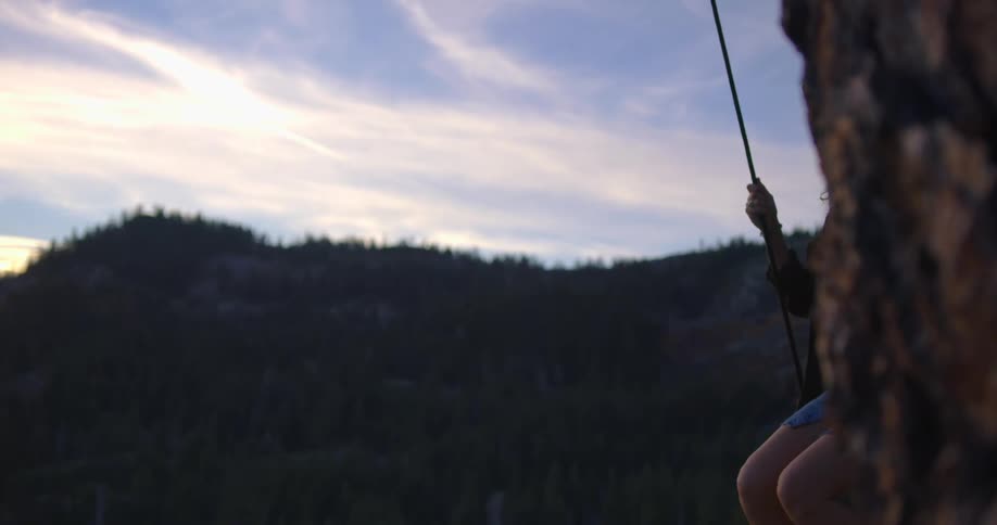 A woman with a hat swinging on a swing with the sky and clouds in the background