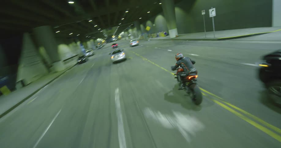 A person rides a motorcycle weaving in between cars in traffic on a street at night