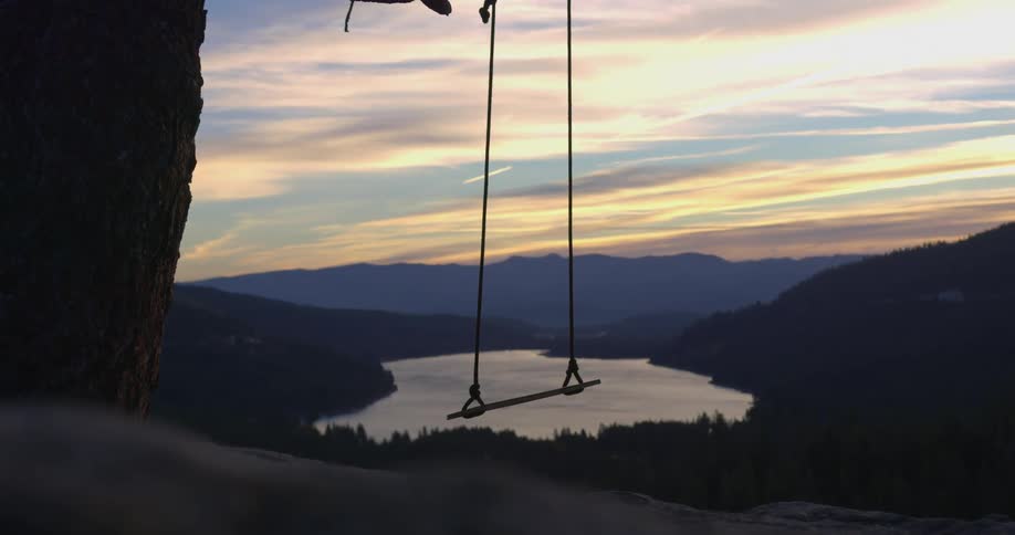 Swing hanging from a tree in front of a lake in the mountains at sunset
