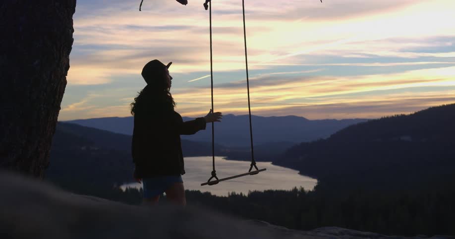 A woman with a hat walking up and grabbing a swing with the sky and clouds in the background