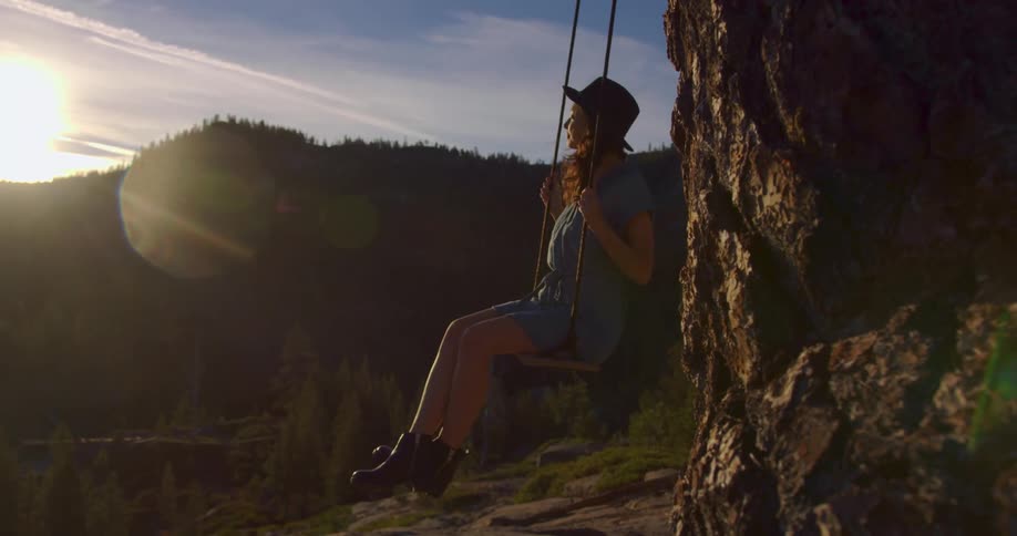 A woman sits on a swing in a forest area above a lake