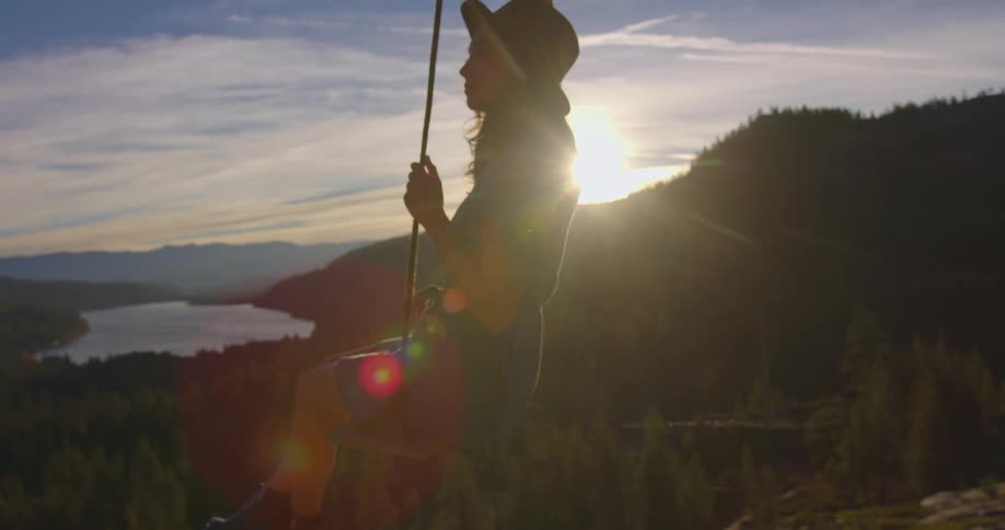 A woman sits on a swing overlooking a forest as the sun rises