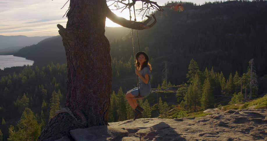 A woman swings on a swing attached to a tree in a forest above a lake
