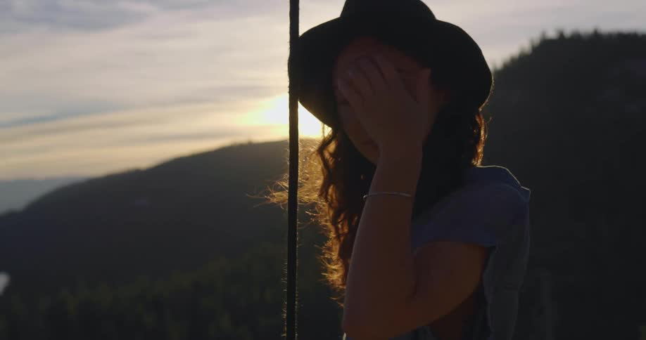 A young woman sits on a swing above a lake and forest at dusk