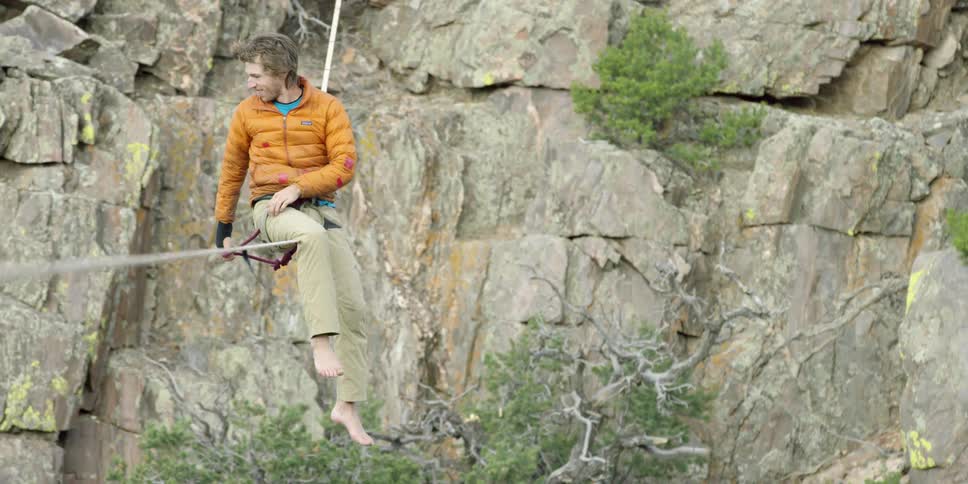 Man sitting and smiling on a tightrope over a canyon