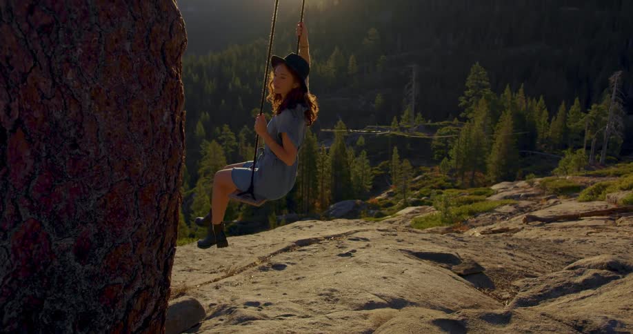A young womans shadow is cast on rock as she swings on an outdoor swing as the sun sets