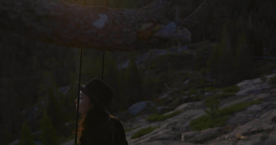 A woman swings on a rope swing hanging from a branch on a rocky hillside