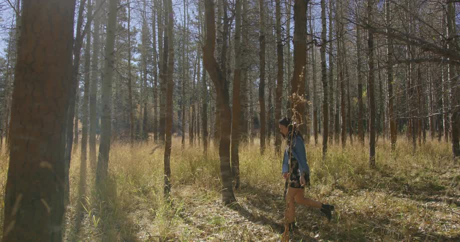 Girl wearing denim jacket and skirt walks through forest on a clear day