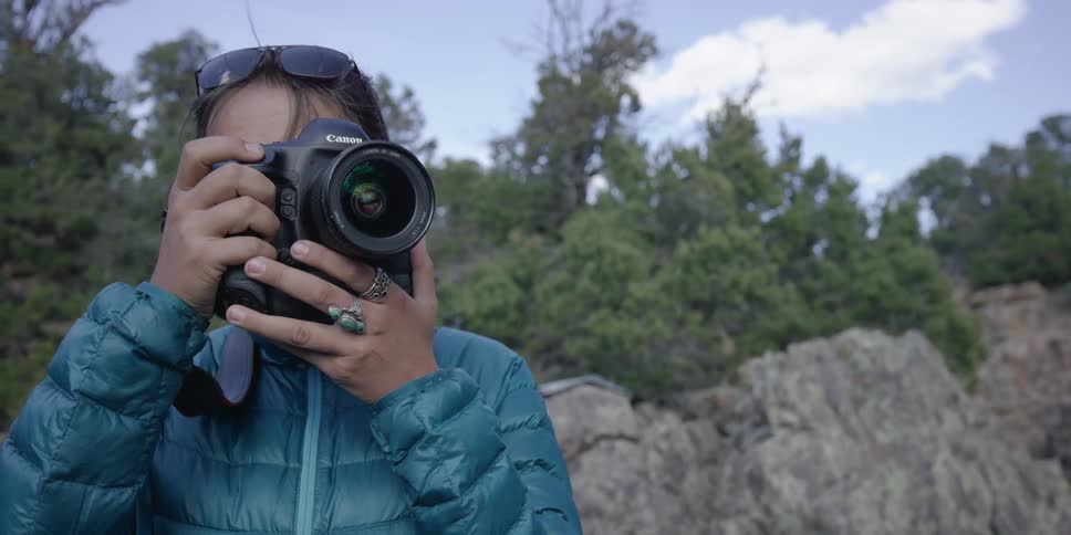 A woman lifts a dslr camera to her eyes and takes pictures