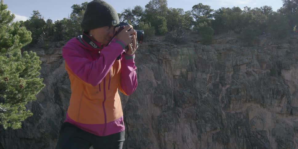 A woman is taking photographs from the edge of a cliff