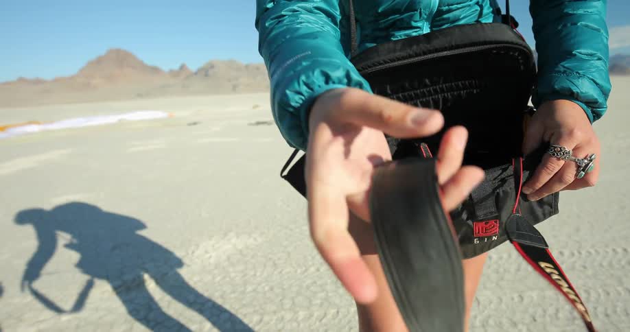 A woman placing a camera in a camera bag and then clipping the camera strap to her coat