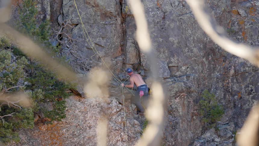 A shirtless man is climbing a rock face