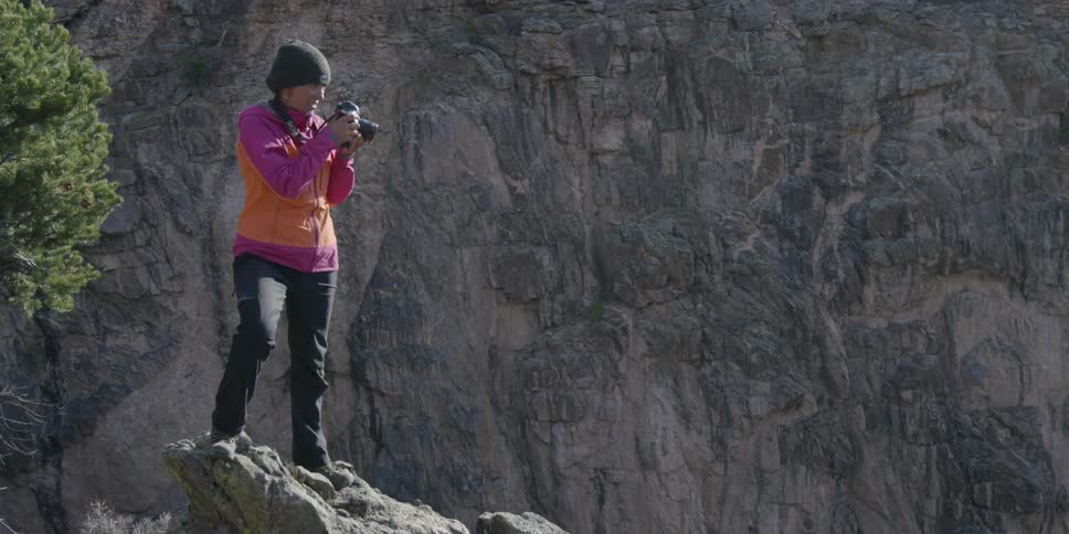 A woman stands on a precipice and takes pictures