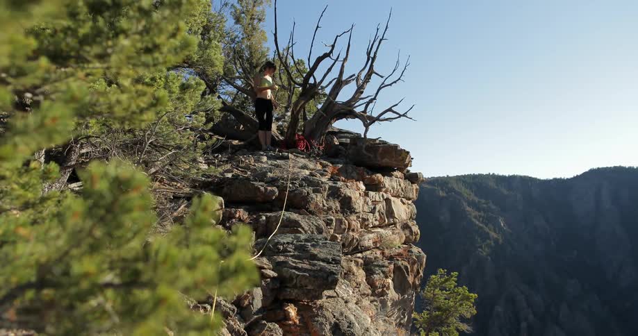 A woman stands on a high precipice with a rope leading away from her
