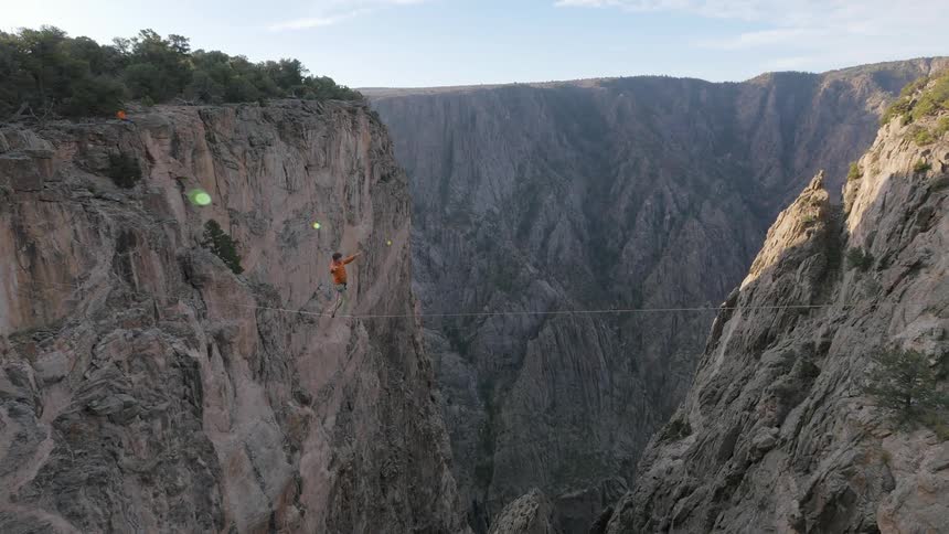 A man walking a tightrope that spans a canyon