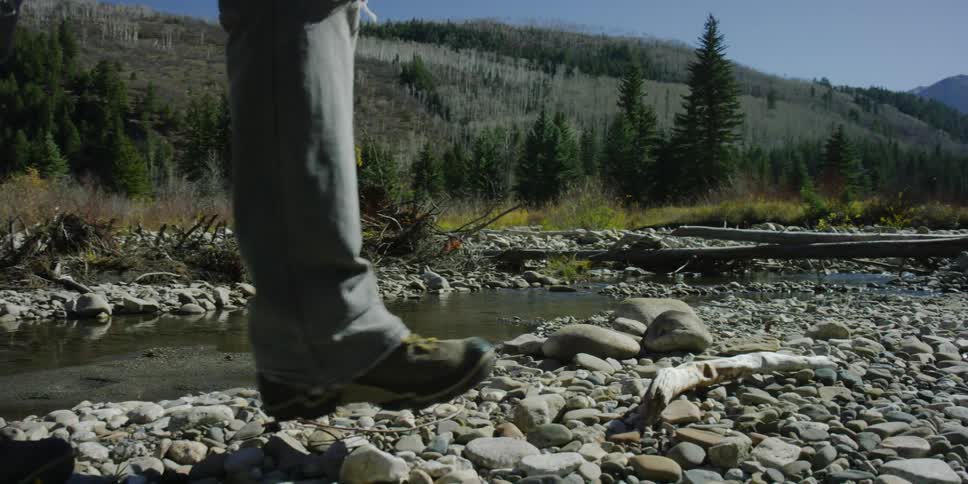 A woman hiking along a rocky creek shoreline in the mountains