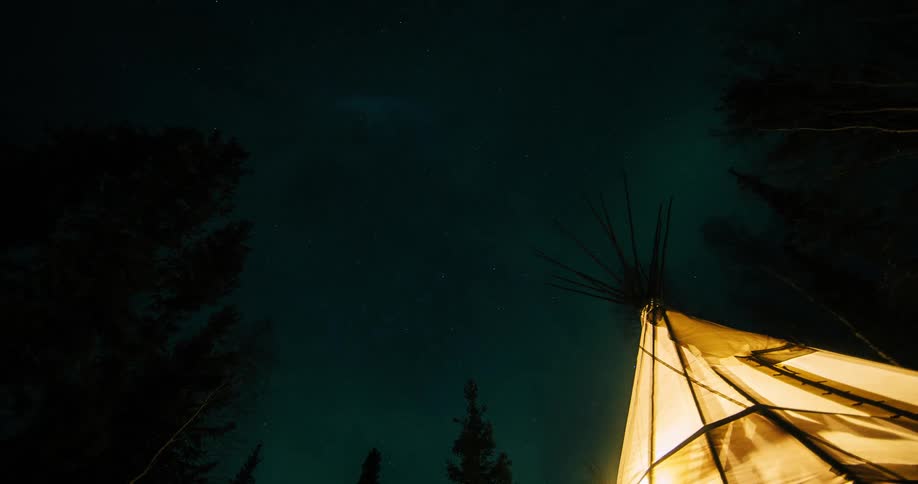 A storm crosses the sky over a lit up tepee